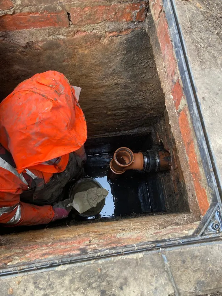 man in orange jacket working on a pipe in a hole