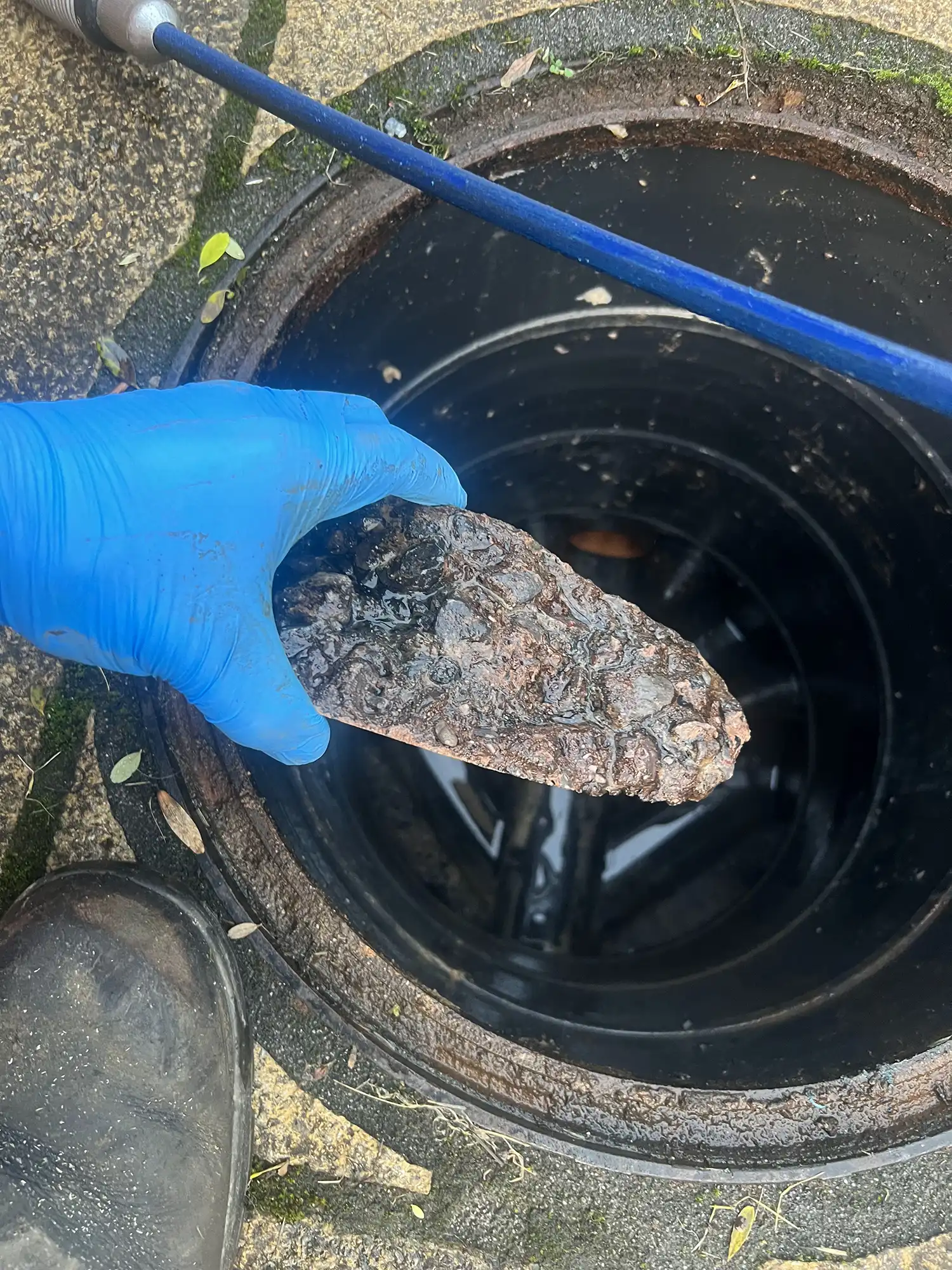 someone is holding a rock in a drain with a blue handle