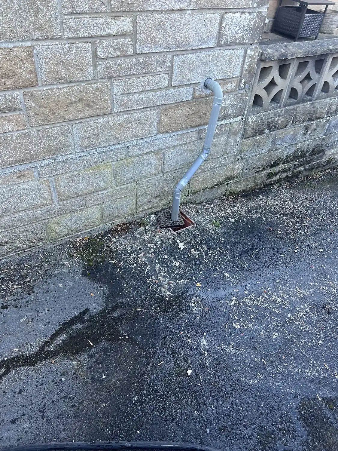 a drain in the street next to a brick wall