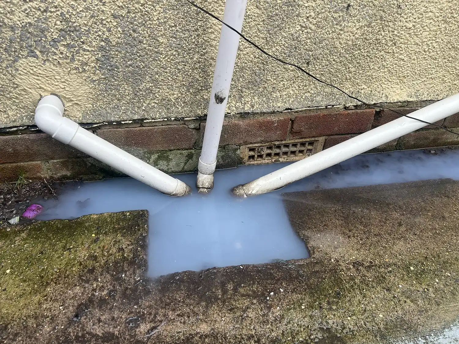 A pipe sticking out of the ground next to a wall.