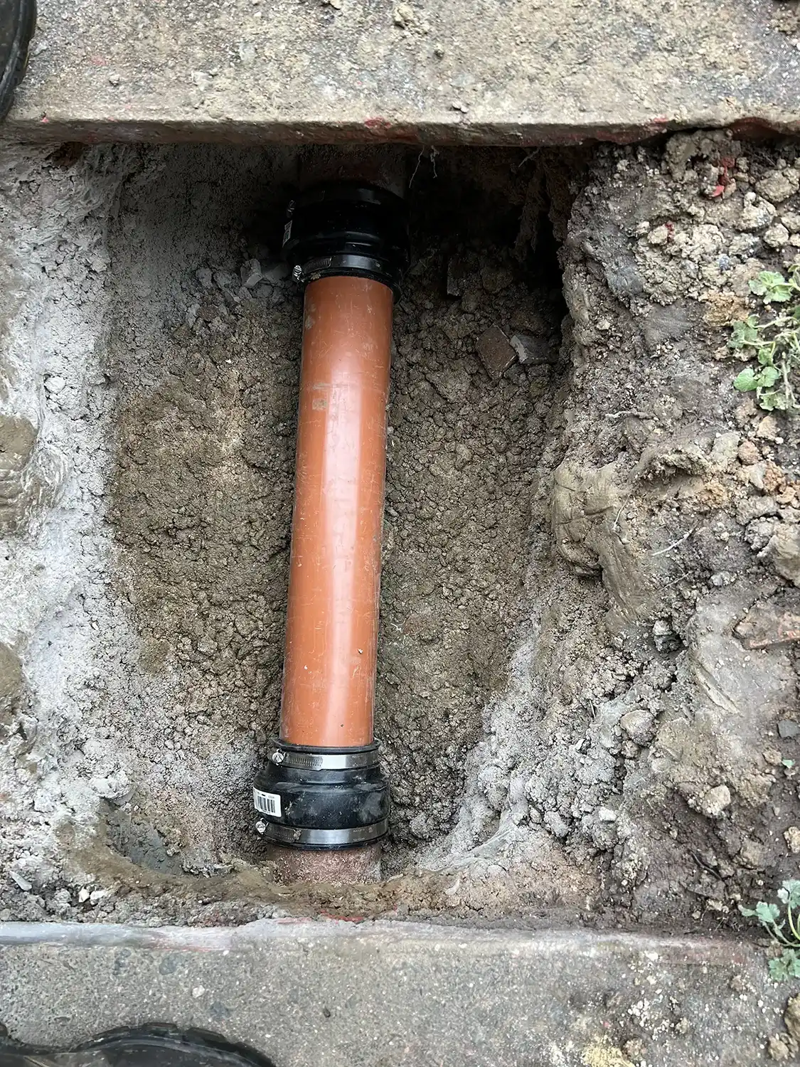 An orange pipe is in a hole in the ground.